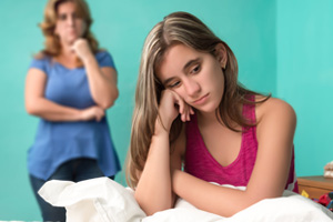Mom looking at depressed teenager sitting on bed